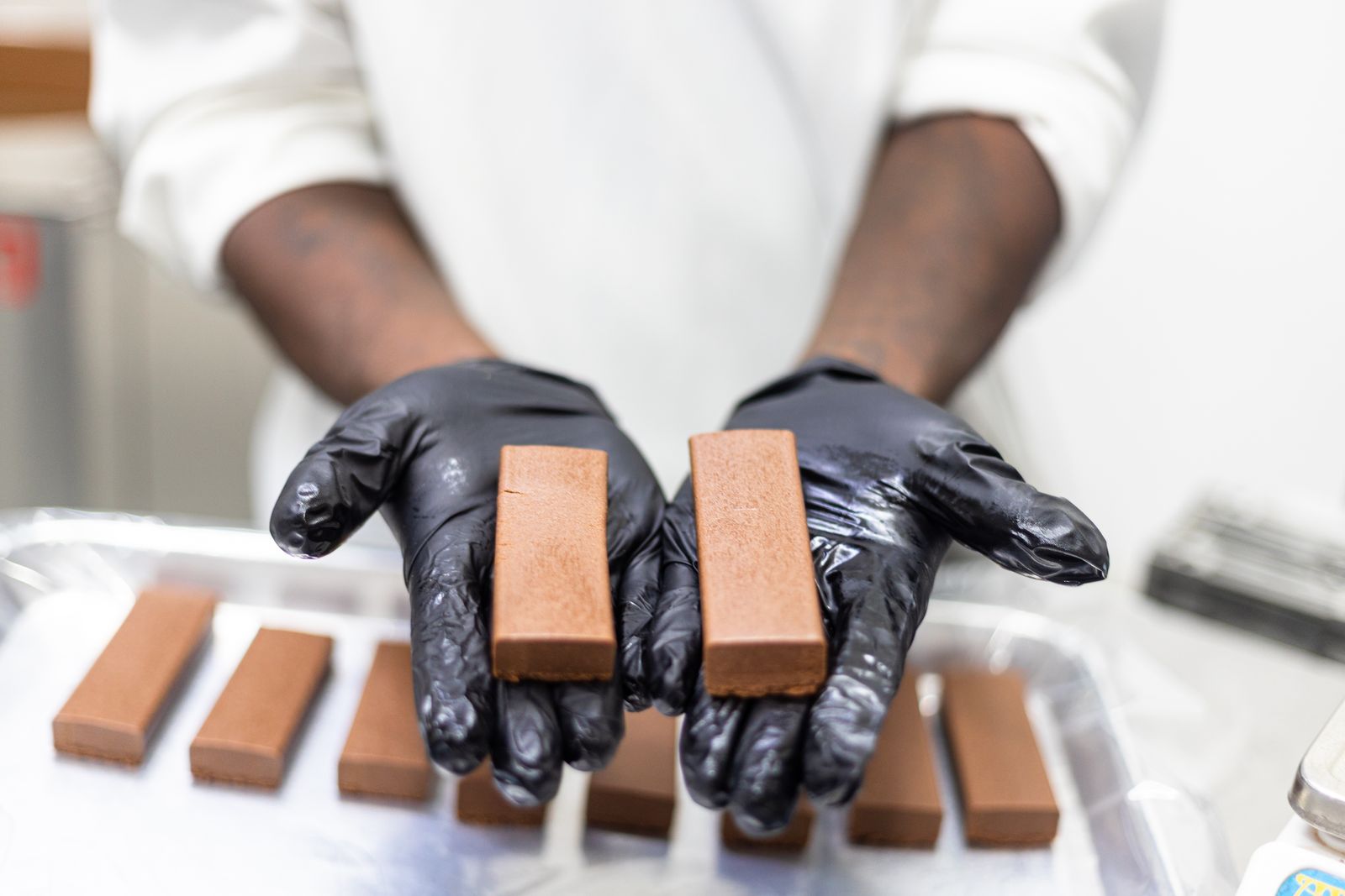 Gloved hands presenting freshly formed cold-extrusion bars for quality checking